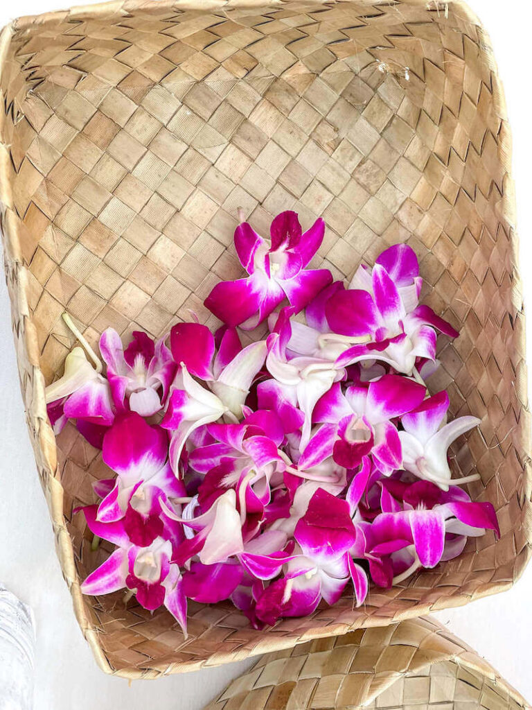 Image of a woven box with purple orchids and lei needles inside.