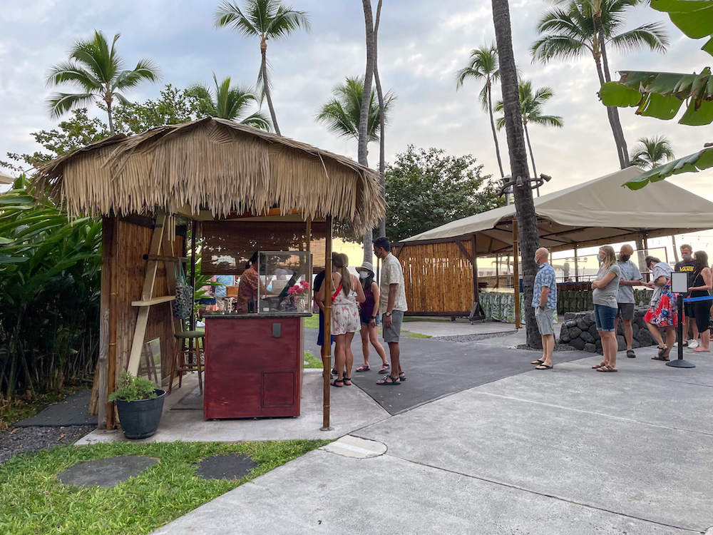 Image of people waiting in line and a check in desk with a thatched roof.