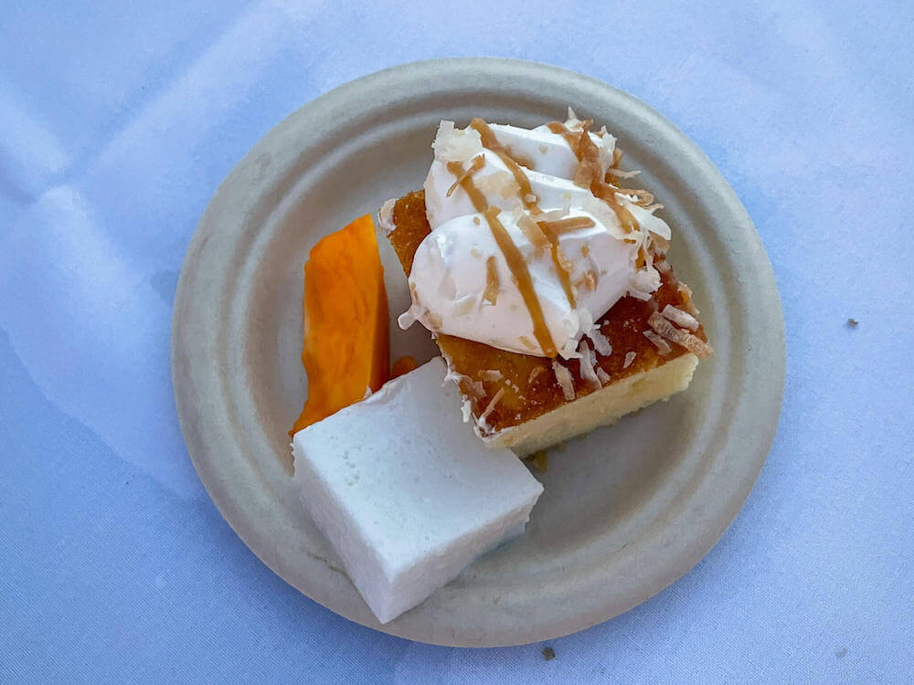 Image of a brown plate with a slice of cake, haupia, and fresh papaya slice.