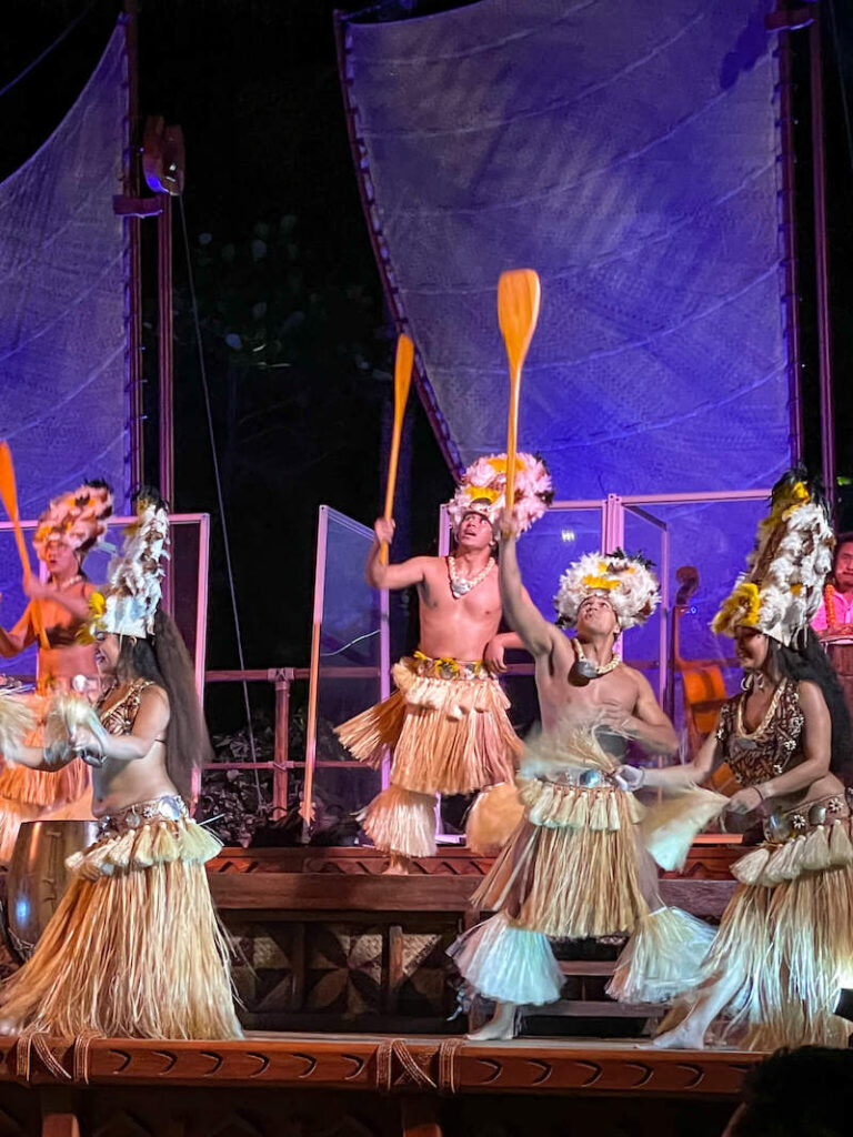 Image of people doing Tahitian dancing wearing feather headdresses and raffia skirts.