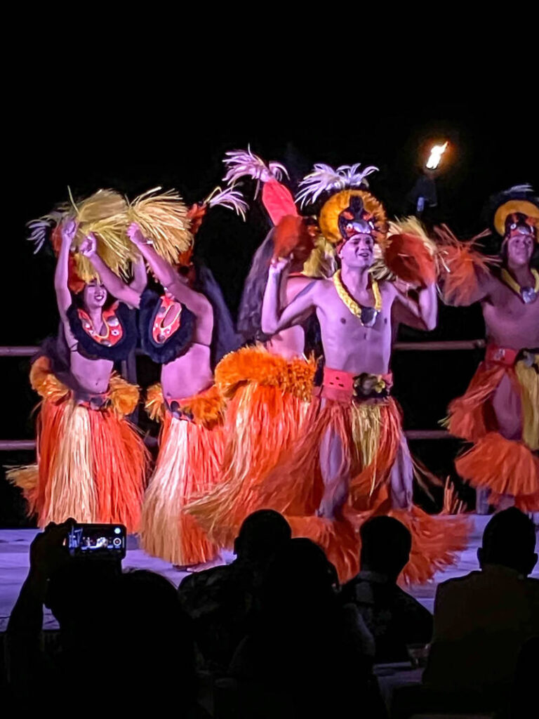 Image of men and women Tahitian dancing in orange costumes.