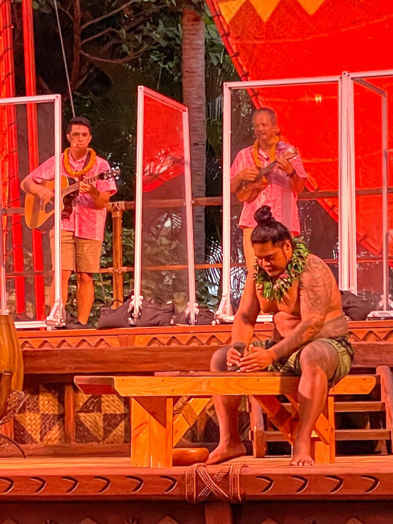 Image of a Polynesian man pounding poi on stage at the Disney Aulani luau on Oahu.