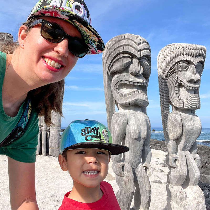 Image of a woman and boy taking a selfie with two tikis at Pu'uhonua o Honaunau National Historical Park on the Big Island of Hawaii.