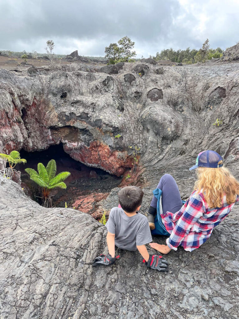 Image of a boy and woman sitting on the edge of a lava cave at Hawaii Volcanoes National Park in Big Island.