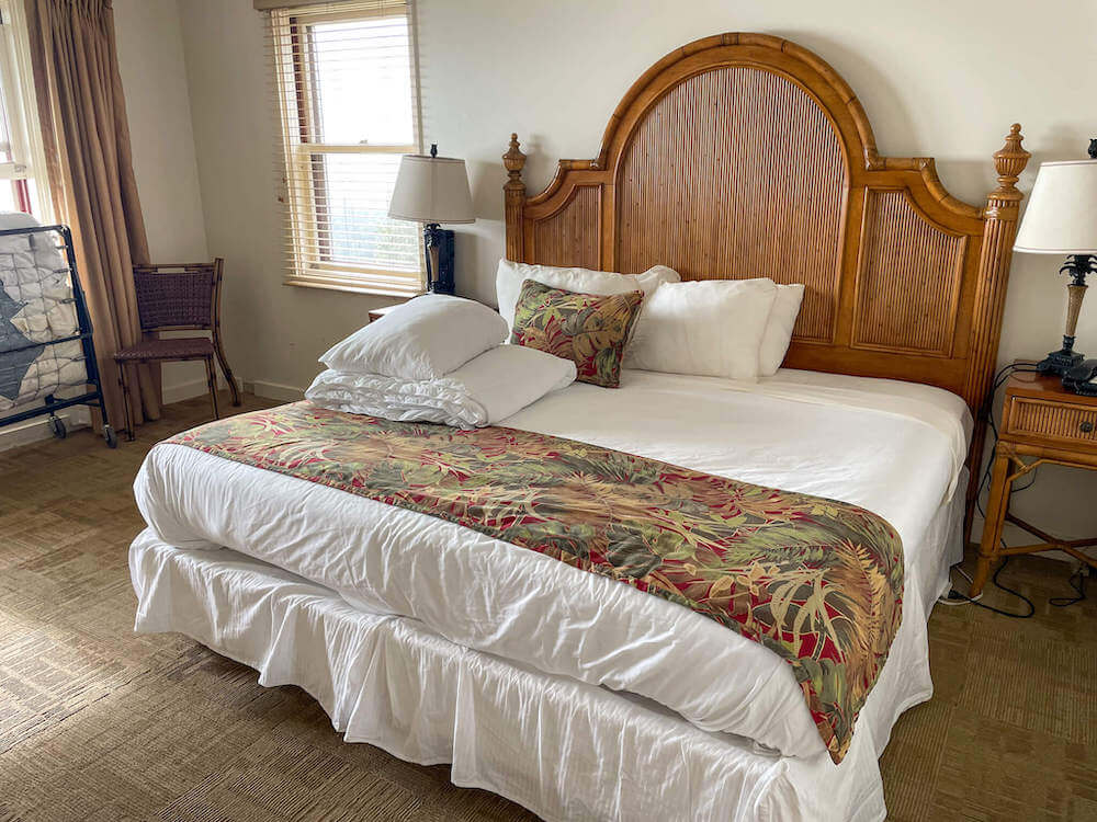 Image of a king size bed with tall wooden headboard and linens folded on top.