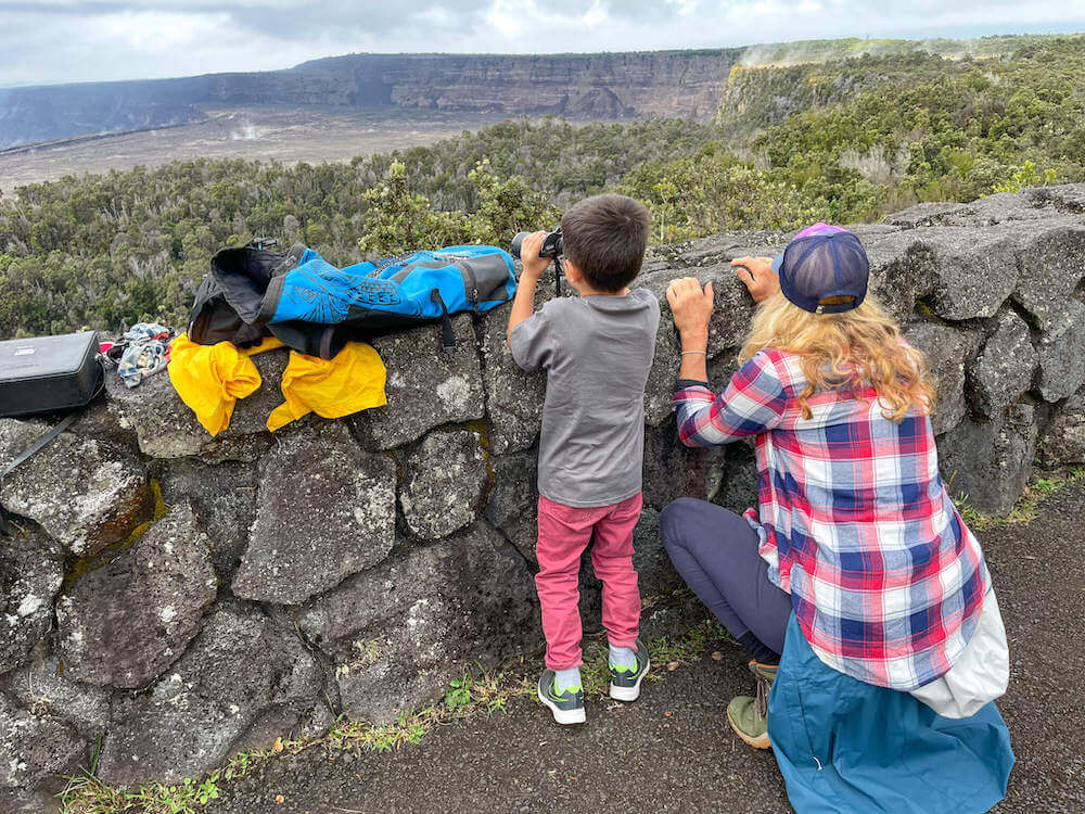 Image of a boy and lady looking over a lava rock wall to see Kilauea crater.