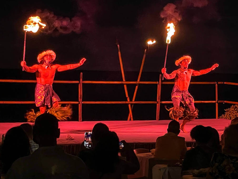 Image of two men holding lit torches dancing on stage at a Kona luau.