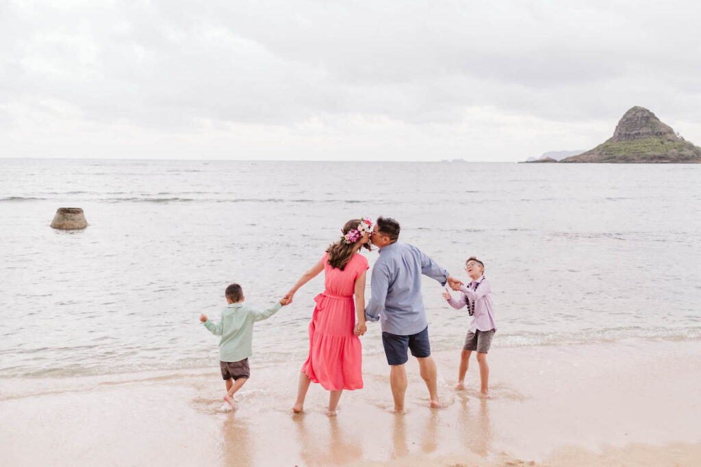 Image of a family holding hands while walking into the water at Kualoa Beach on Oahu