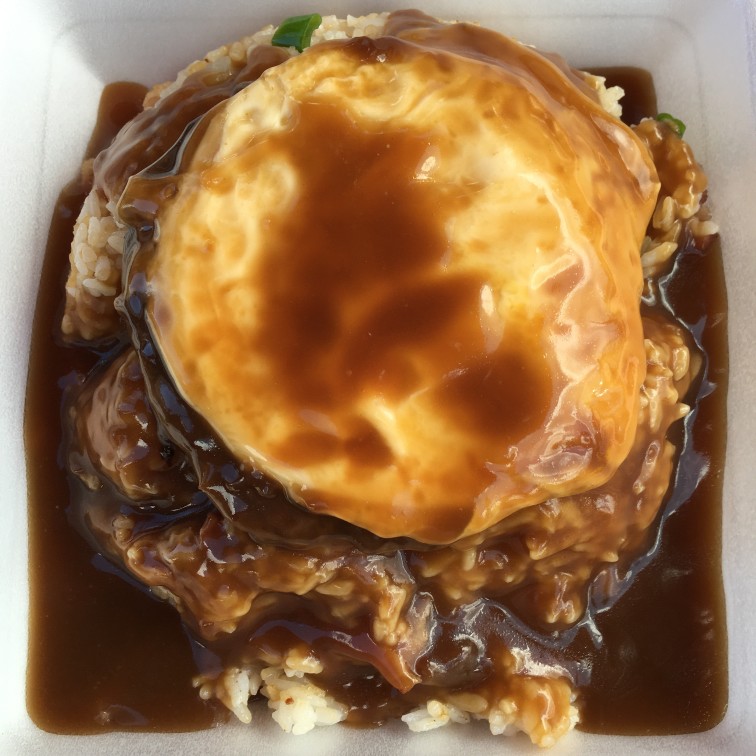 Image of a fried egg on top of a hamburger patty, on a bed of rice, smothered in brown gravy.