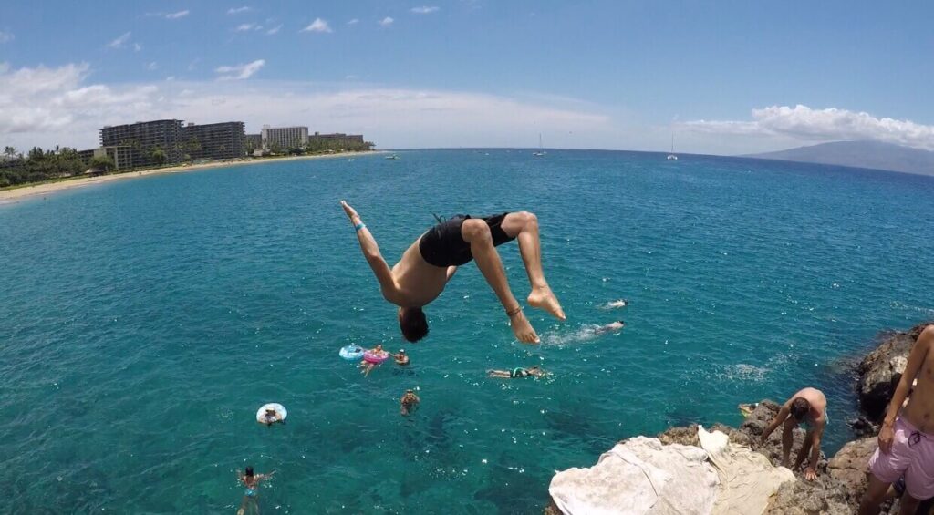 Image of a man doing a flip as he cliff dives at Black Rock Beach in Maui.