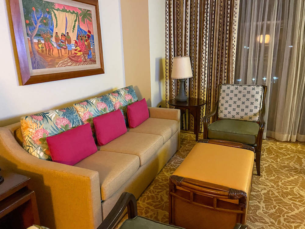 Image of a beige couch, green chair, coffee table and Hawaiian artwork at Disney Aulani Villa.