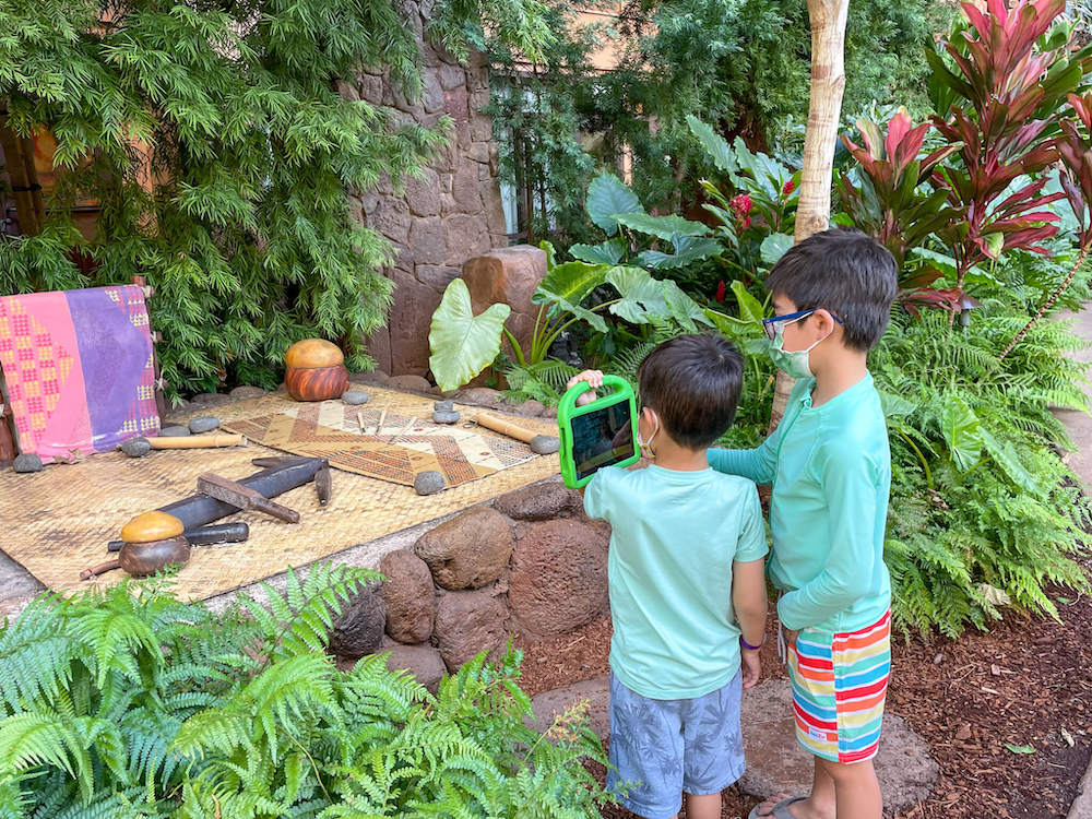 Image of two boys holding a green iPad in front of Hawaiian instruments.