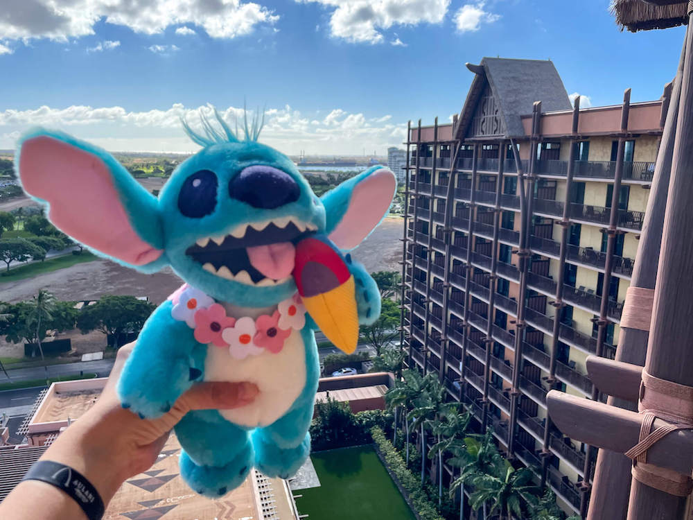 Image of a plush Stitch doll eating shave ice with Aulani Resort in the background.