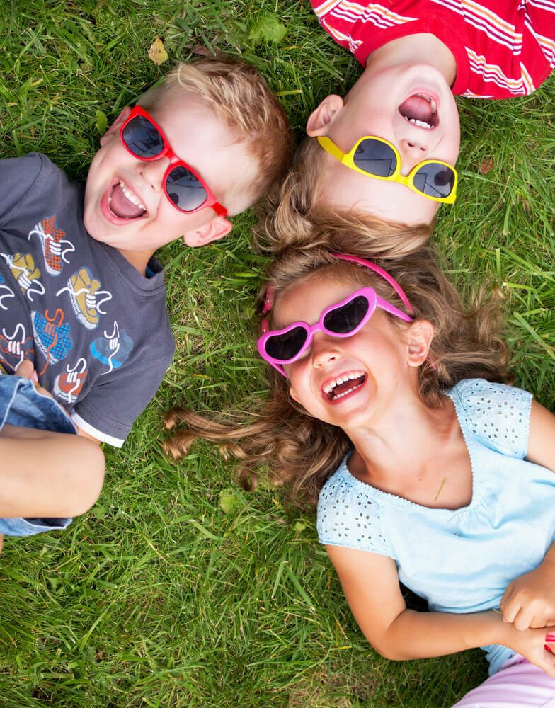 Find out the funniest jokes about Hawaii for kids by top Hawaii blog Hawaii Travel with Kids. Image of 3 kids laying in the grass laughing together.