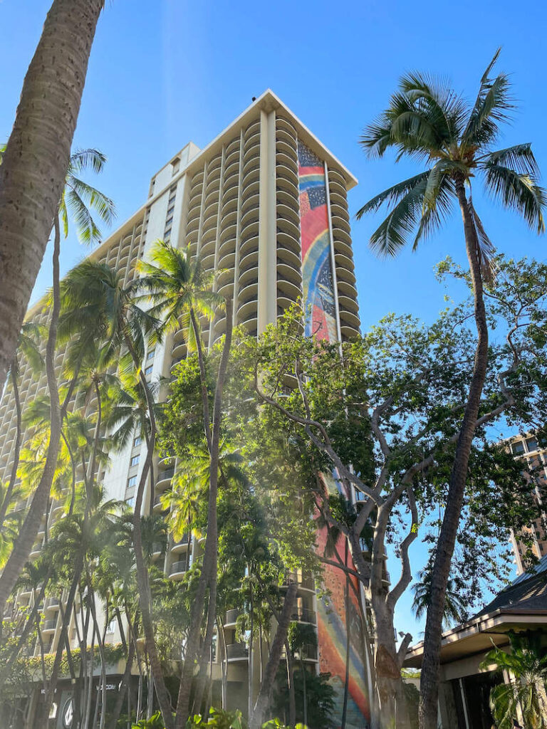 Image of a tall hotel tower with a bit rainbow mural painted on the side. This is one of the best places to stay in Waikiki with kids.