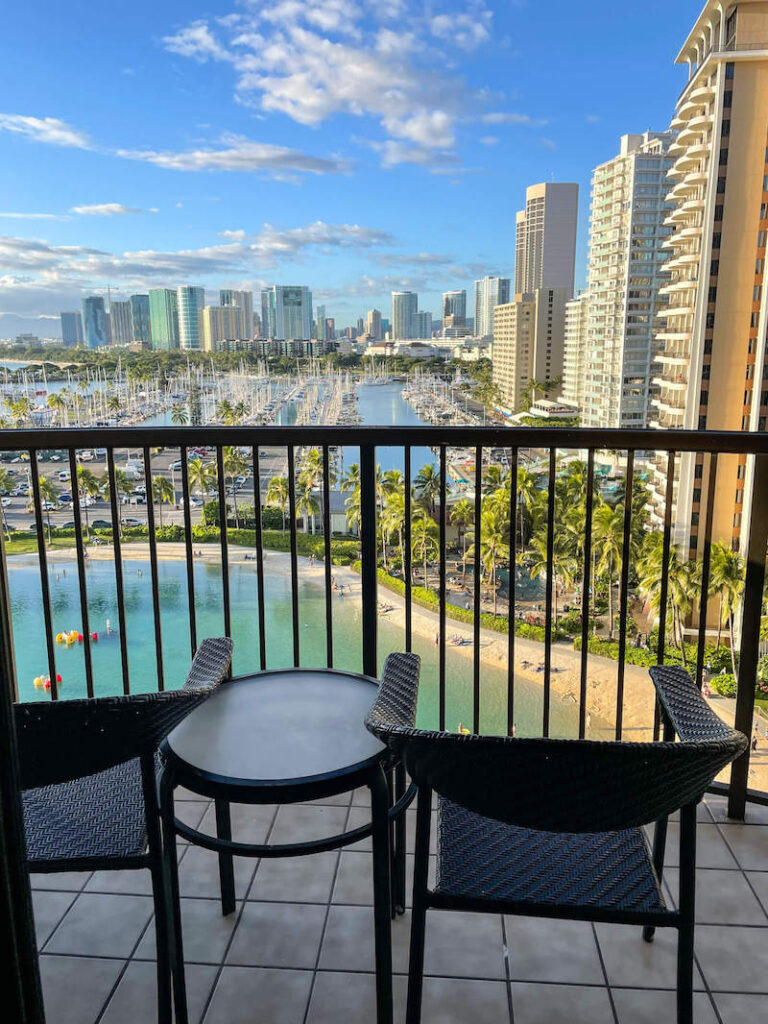 Image of two outdoor chairs on a lanai overlooking the Hilton Hawaiian Village lagoon and Honolulu.