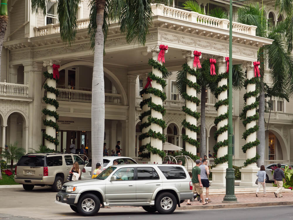 Image of a white hotel with tall columns with greenery wrapped around it with red bows during Christmas on Oahu Hawaii.