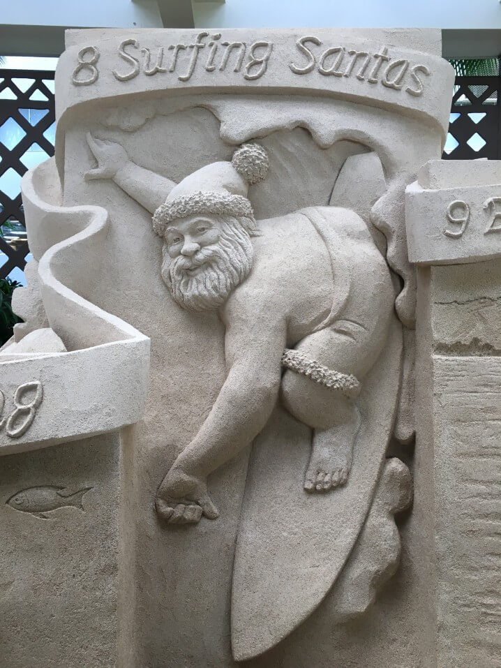 Image of a sand sculpture of 8 surfing Santas at the Sheraton Waikiki during Christmas in Hawaii.