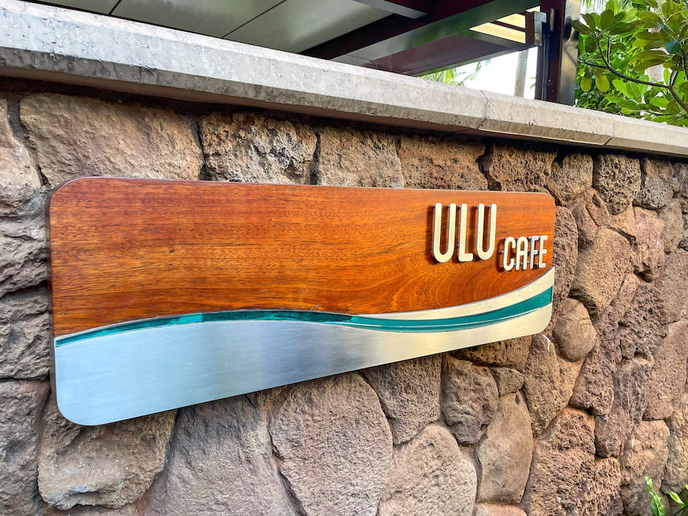 Image of a wood sign that says Ulu Cafe on a rock wall.