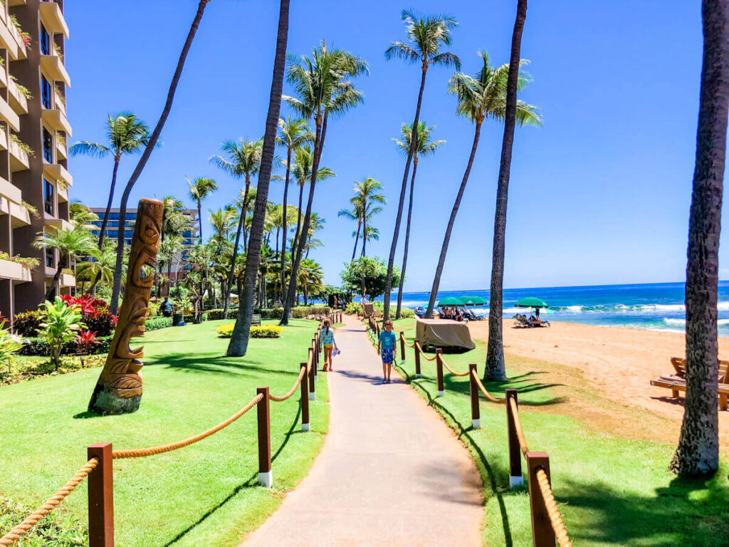 Image of two kids walking on a paved path next to the beach in Kaanapali Maui.