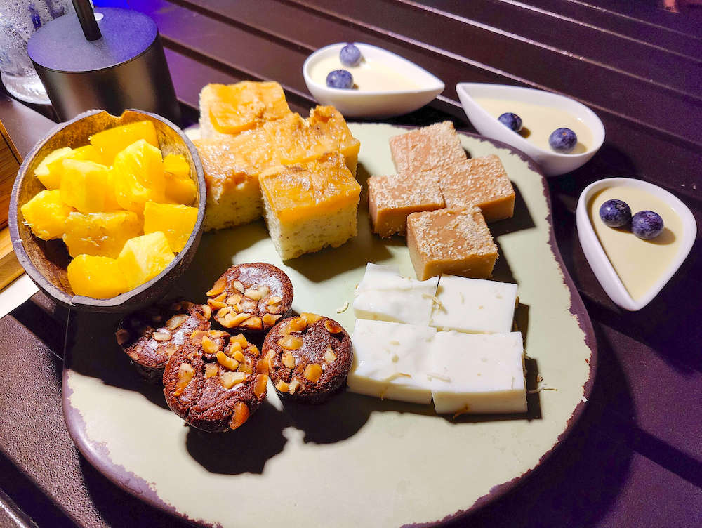 Image of a tray of coconut pudding squares, chopped pineapple, and other treats at a luau in Maui.