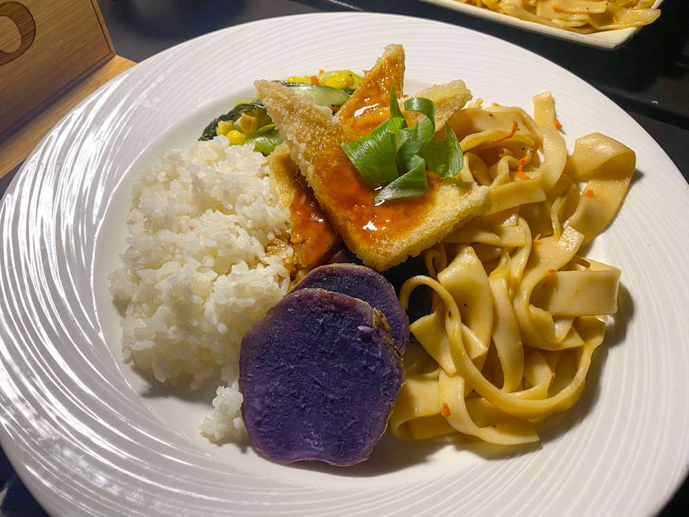 Image of a plate of Hawaiian food at a Maui luau. Items include noodles, purple potatoes, and rice.