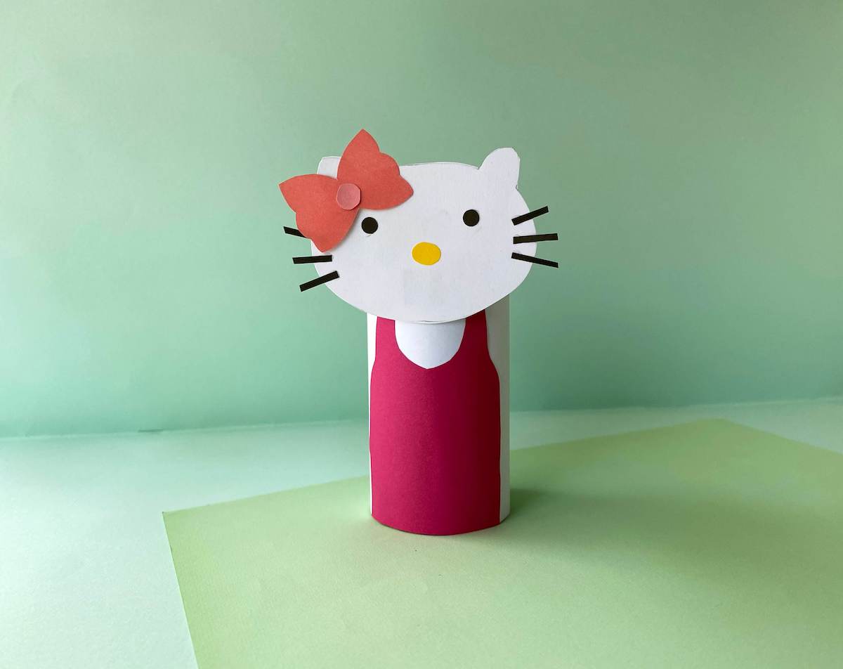 Learn how to make this Hello Kitty Craft by top Hawaii blog Hawaii Travel with Kids. Image of a Hello Kitty Sanrio Paper Craft with a green background.