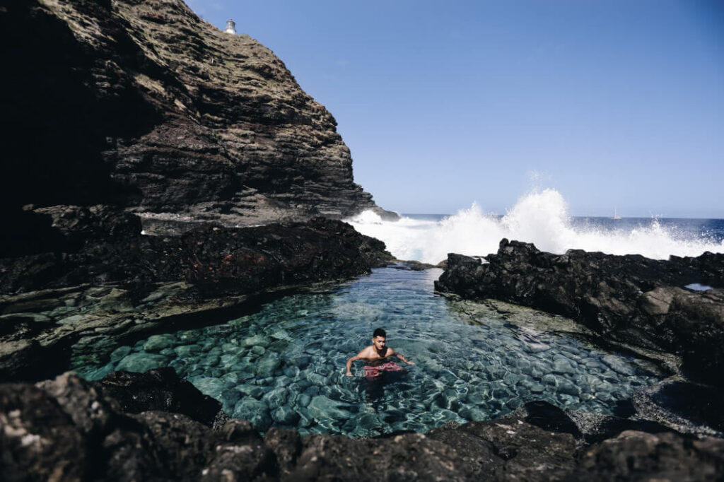 Image of a man swimming in a tidepool surrounded by lava rocks on Oahu