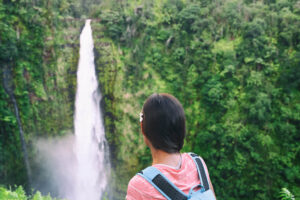 Find out the best Big Island waterfall hikes by top Hawaii blog Hawaii Travel with Kids. Image of a woman wearing a backpack staring at Akaka Falls near Hilo Hawaii