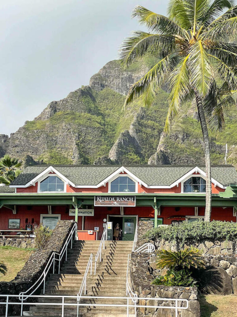 Image of a red ranch with a bunch of concrete stairs in front and green mountains in the background.