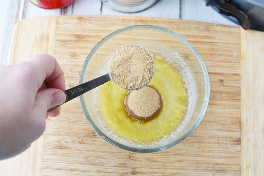 Image of someone adding brown sugar to a bowl of melted butter.