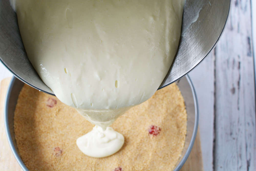 Image of someone pouring a creamy mixture on top of a graham cracker crust.