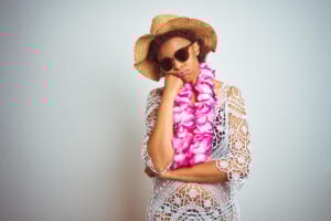 Find out the worst time to visit Hawaii by top Hawaii blog Hawaii Travel with Kids. Image of a woman wearing a straw hat and purple lei looking disappointed with her chin on her hand.