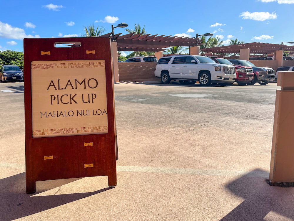 Image of a little Alamo Pick Up sandwich board with rental cars in the background