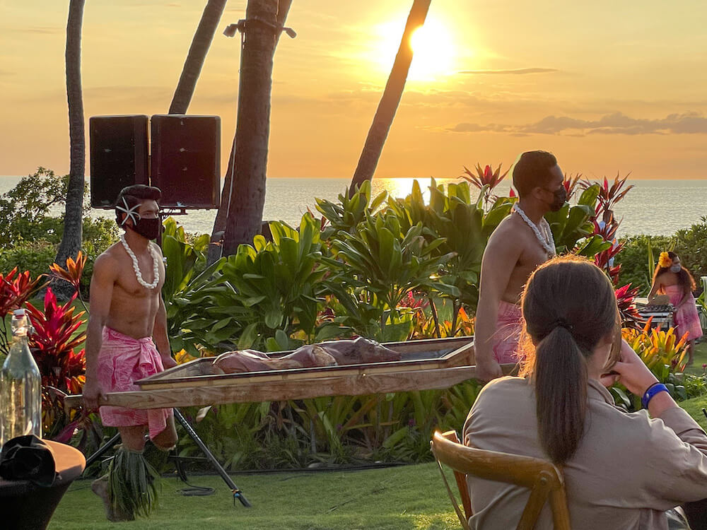 Image of two men carrying a roasted pig at sunset in Hawaii