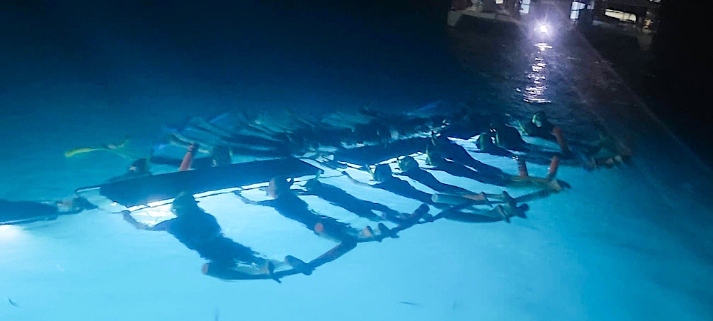 Image of snorkelers holing onto a long flotation device while they swim with Manta Rays in Hawaii.