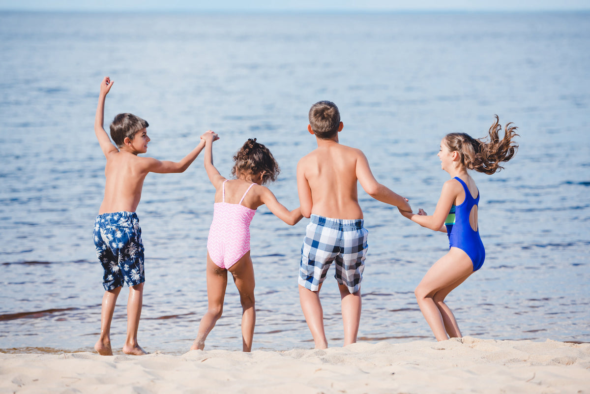 Find out whether Big Island vs Kauai is the best Hawaiian Island with kids by top Hawaii blog Hawaii Travel with Kids! Image of four kids jumping on the beach