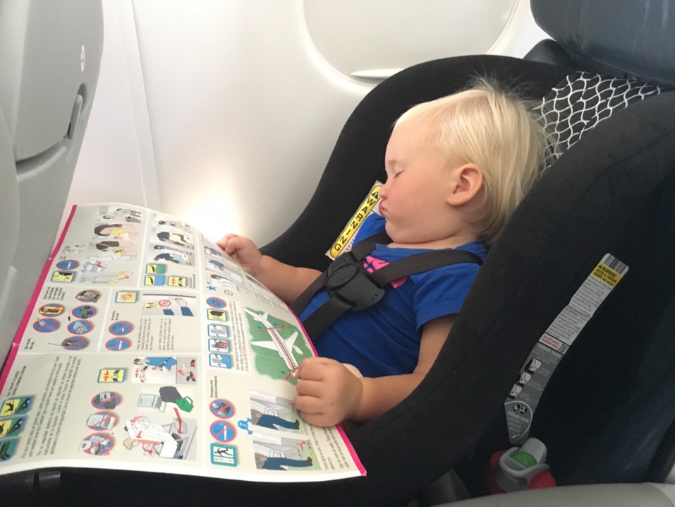 Image of a blonde baby in a car seat on an airplane.