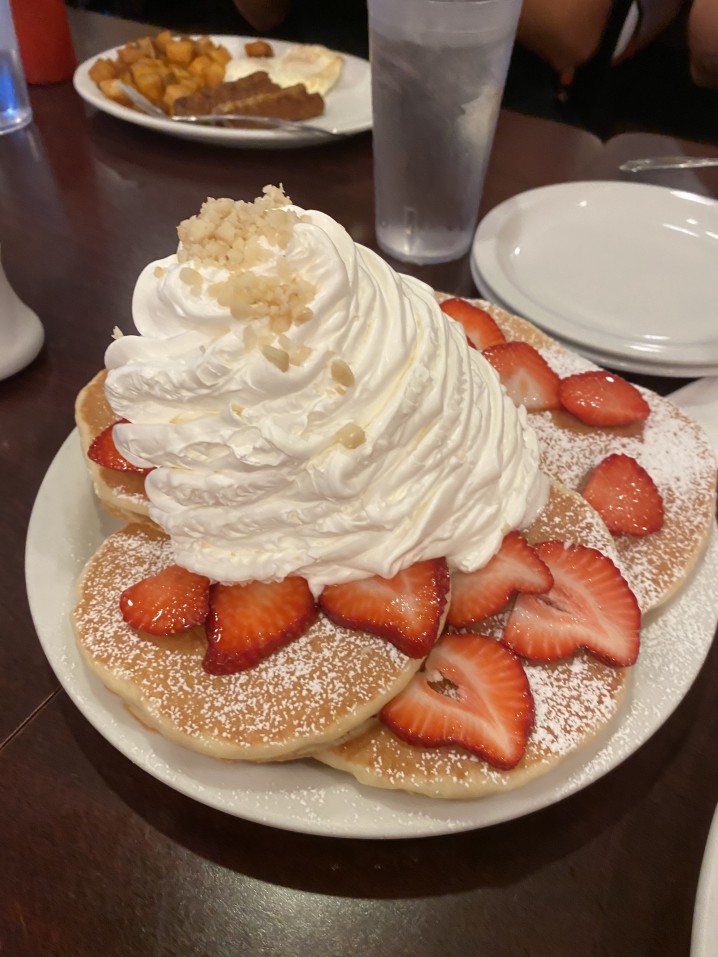 Image of a plate of pancakes with slices strawberries and LOTS of whipped cream.