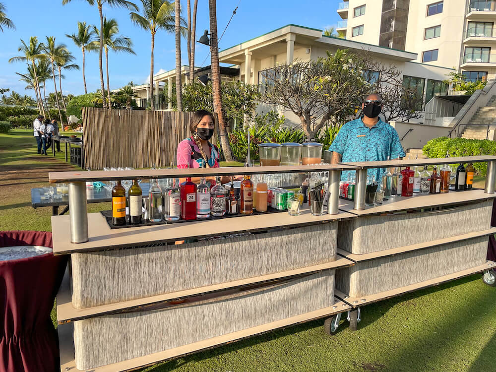 Image of two people wearing face masks standing behind an outdoor bar in Maui
