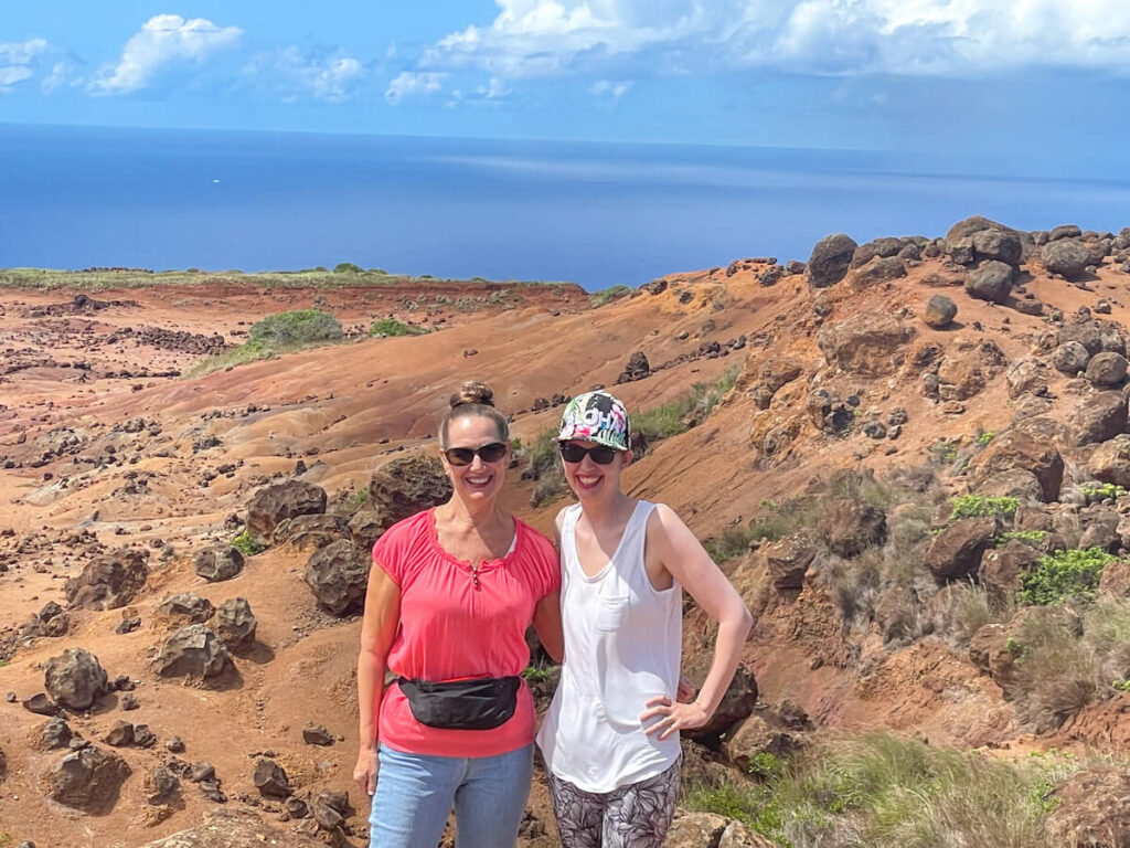 Image of two women posing with a rocky hillside and the ocean in the background at Garden of the Gods in Lanai.