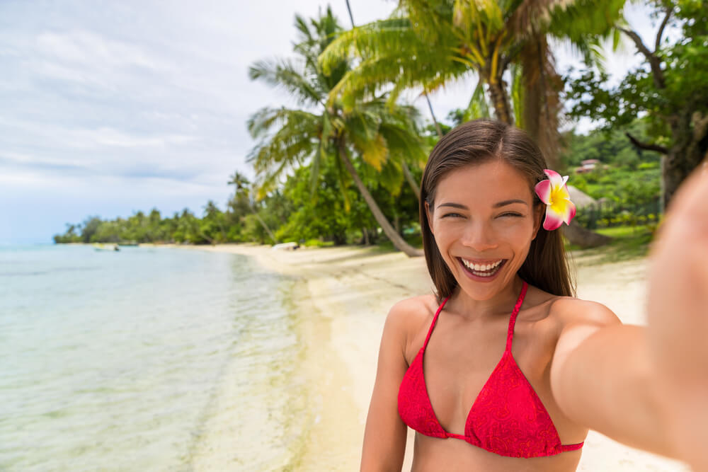 Image of a woman wearing a red bikini taking a selfie at the beach in Hawaii.