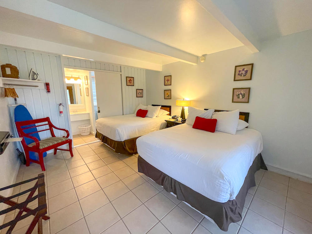 Image of two beds in a white hotel room with a little kitchenette.