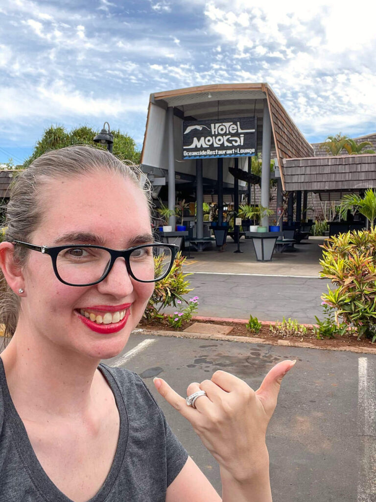 Image of a woman taking a selfie throwing a shaka in front of the Hotel Moloka'i sign.