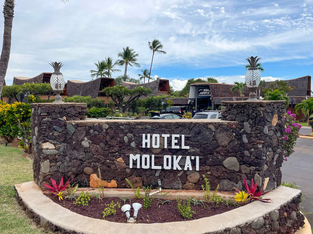 Image of a lava rock sign that says Hotel Moloka'i with the hotel in the background.