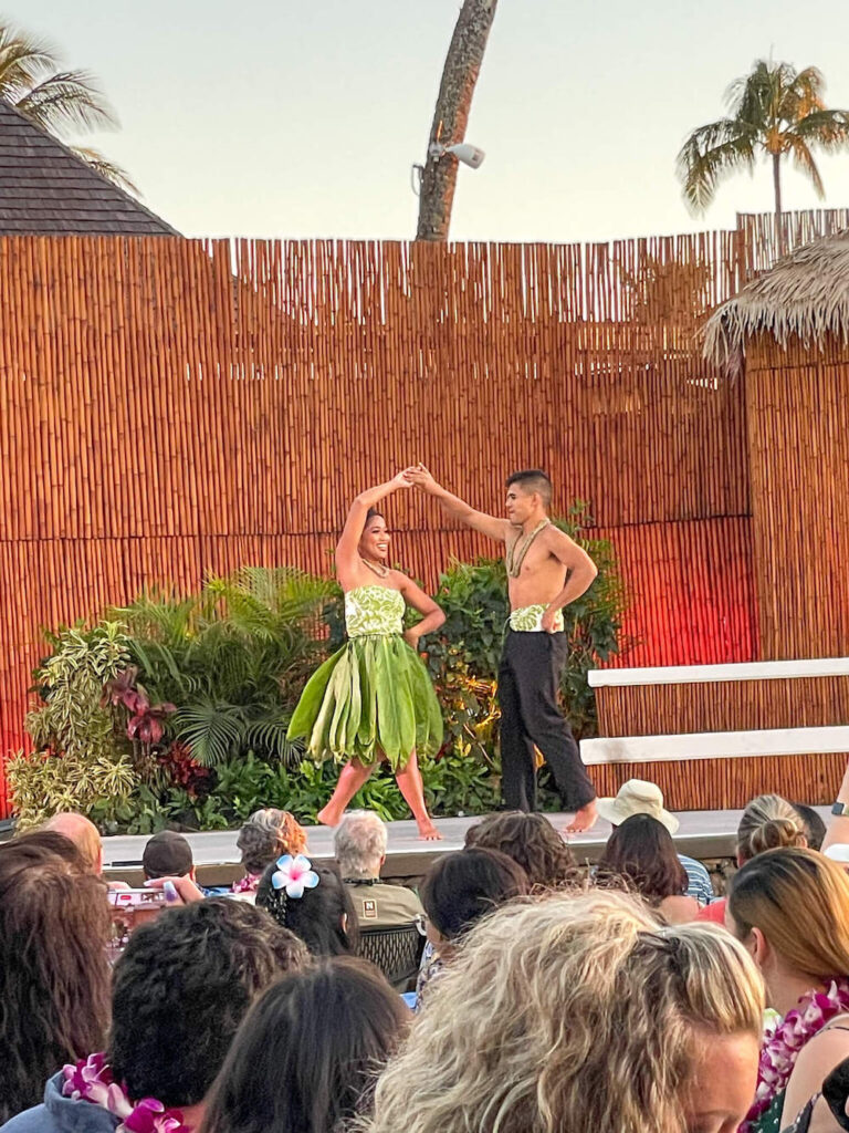 Image of a woman wearing a ti leaf skirt and a man wearing black pants and a bare chest hula dancing at the Royal Lahaina luau on Maui.