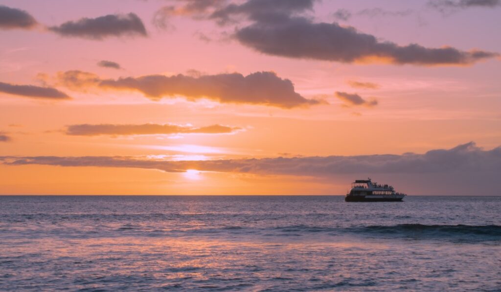 Image of sunset over the ocean with a tour boat in the foreground