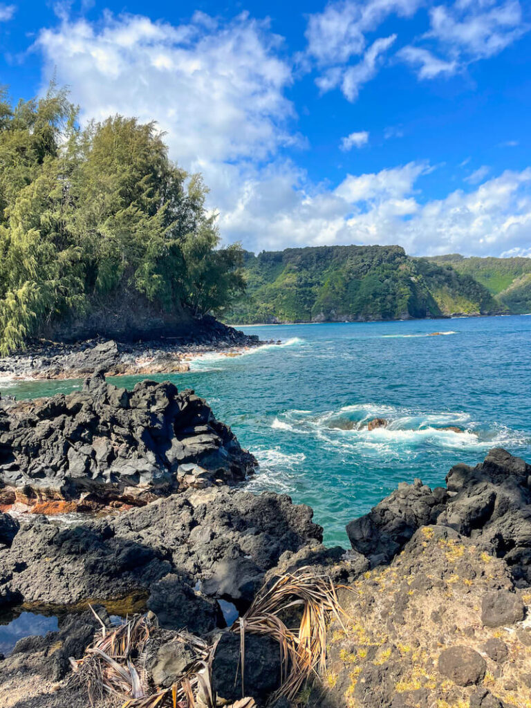 Image of rocks and ocean with green cliffs in the background at Keanae Peninsula on Maui.