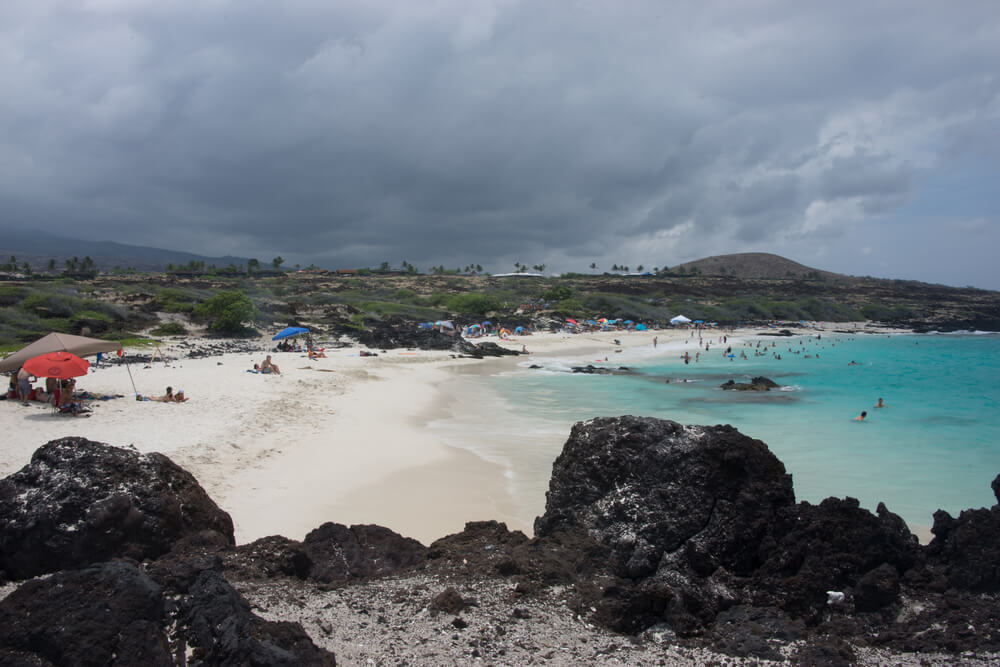 Image of a Big Island beach with white sand and lots of lava rocks.