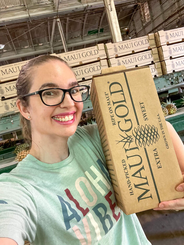 Image of a lady wearing glasses doing a selfie with a Maui Gold pineapple box